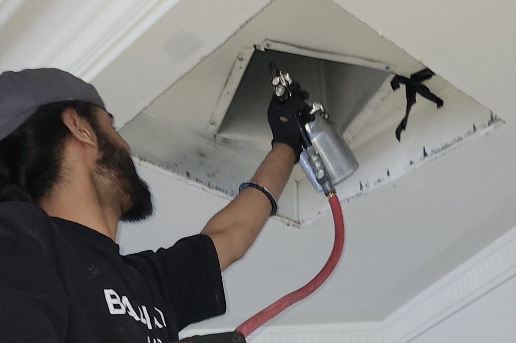 A technician directs compressed air into a vent opening, ensuring thorough removal of dust and allergens for better airflow.