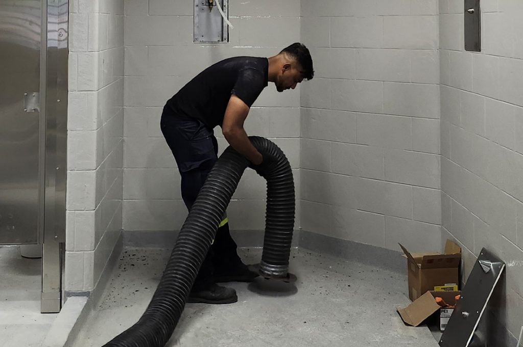 A duct cleaning specialist uses a large vacuum hose to remove debris and improve indoor air quality in a commercial facility.